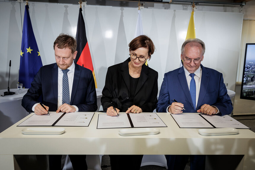 Drei Personen unterzeichnen an einem Tisch eine Vereinbarung